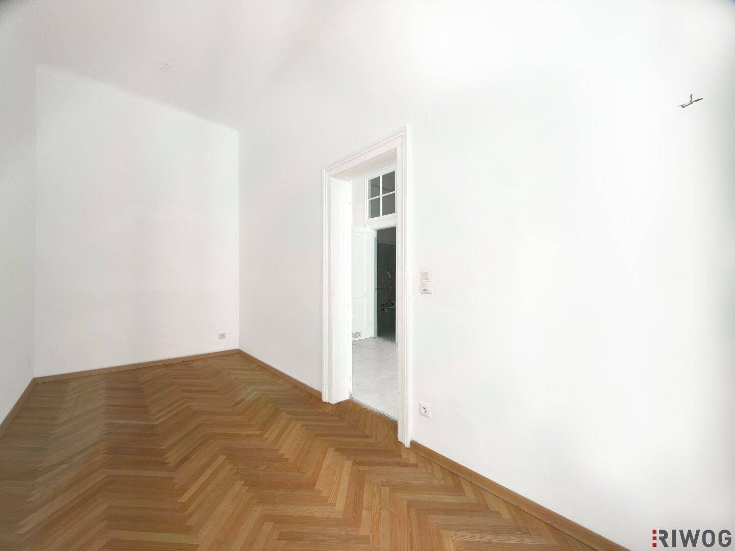 Gemütliches Zimmer mit Fischgrätparkett und einer Tür, die zu einem weiteren Raum führt.