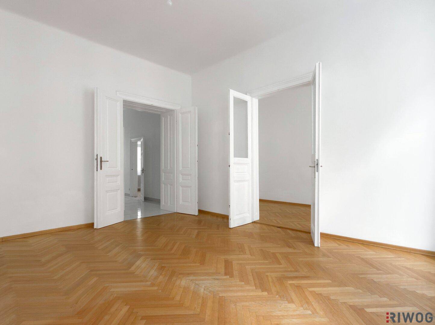 Geräumiges Zimmer mit Fischgrätparkett und mehreren Türen, das vielseitige Nutzungsmöglichkeiten bietet.