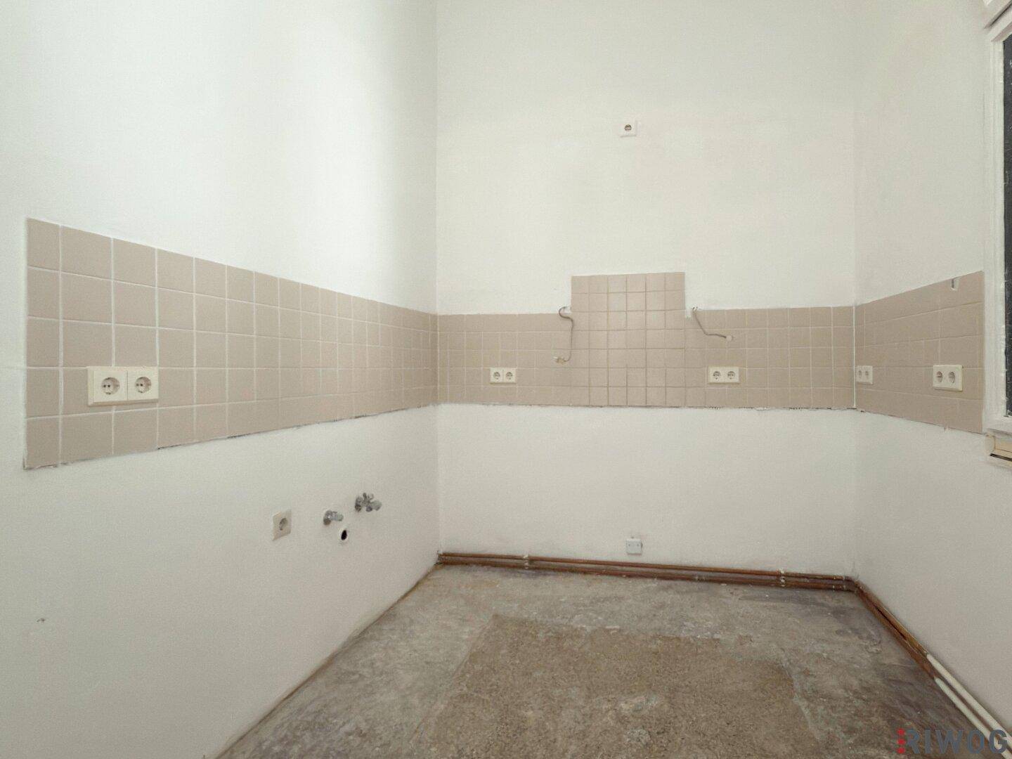 Helle Küche mit Fliesenrückwand und vorbereiteten Anschlüssen für Küchengeräte.