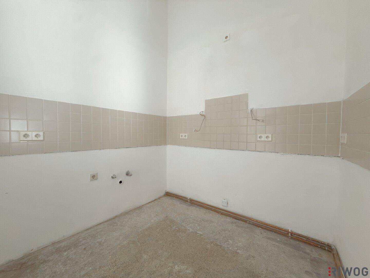 Unmöblierte Küche mit Fliesenrückwand und Anschlüssen, ideal für eine individuelle Küchenplanung.