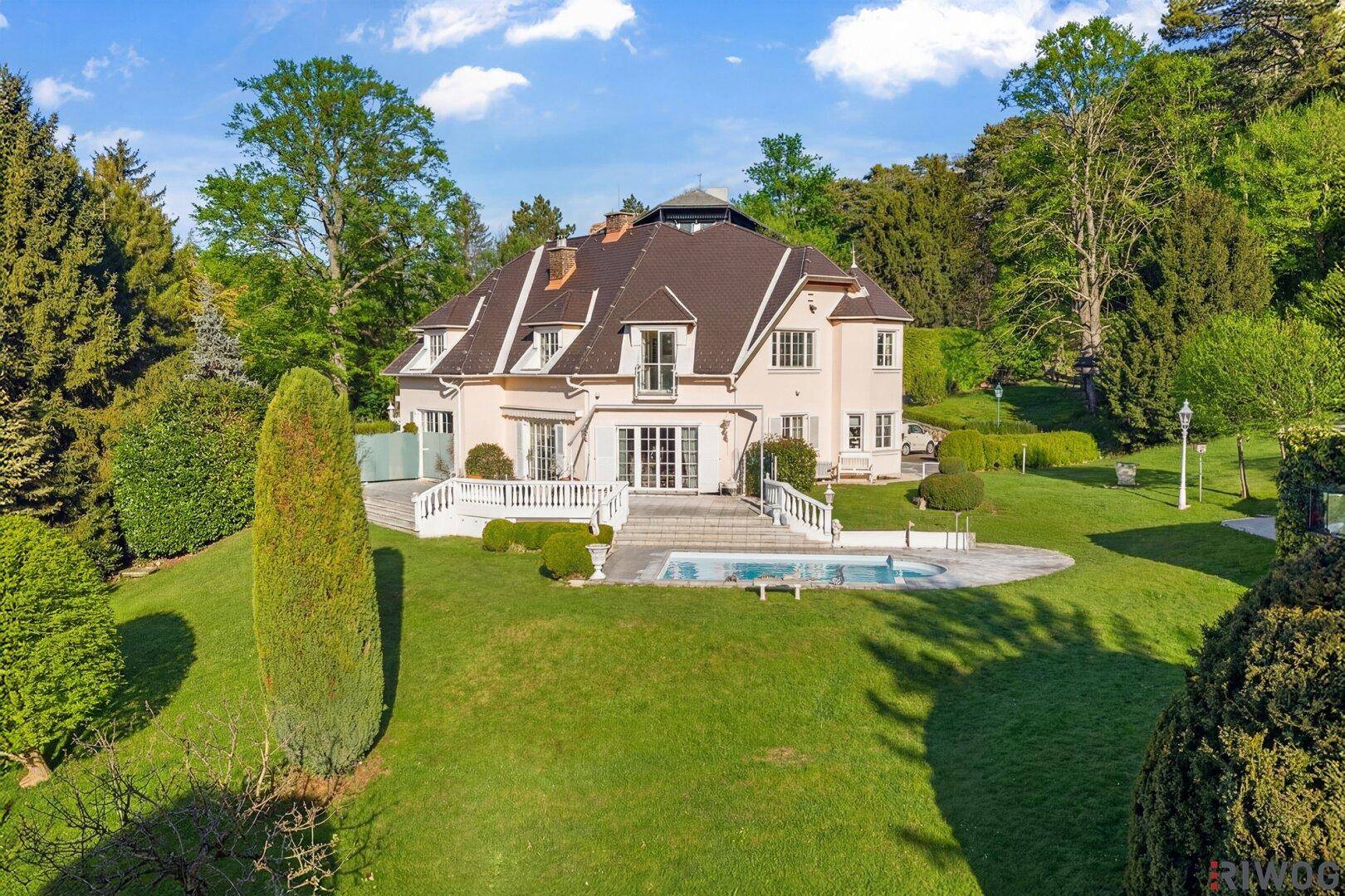 Elegante Villa mit weitläufigem Garten, privatem Pool und gepflegter Grünanlage unter blauem Himmel.