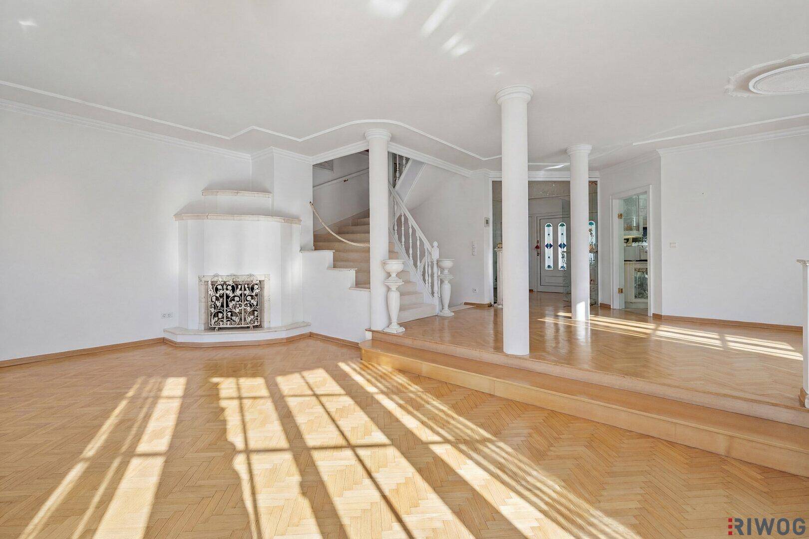 Helles Wohnzimmer mit Fischgrätparkett, Kachelofen und Zugang zu einer Treppe.