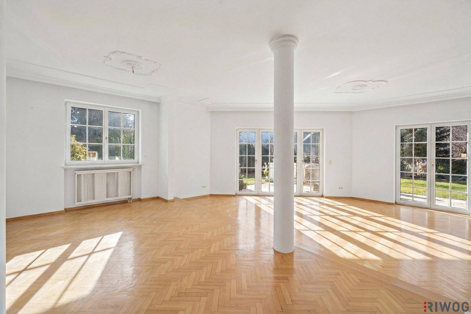 Geräumiges Wohnzimmer mit Fischgrätparkett, großen Fenstern und Zugang zum Garten.