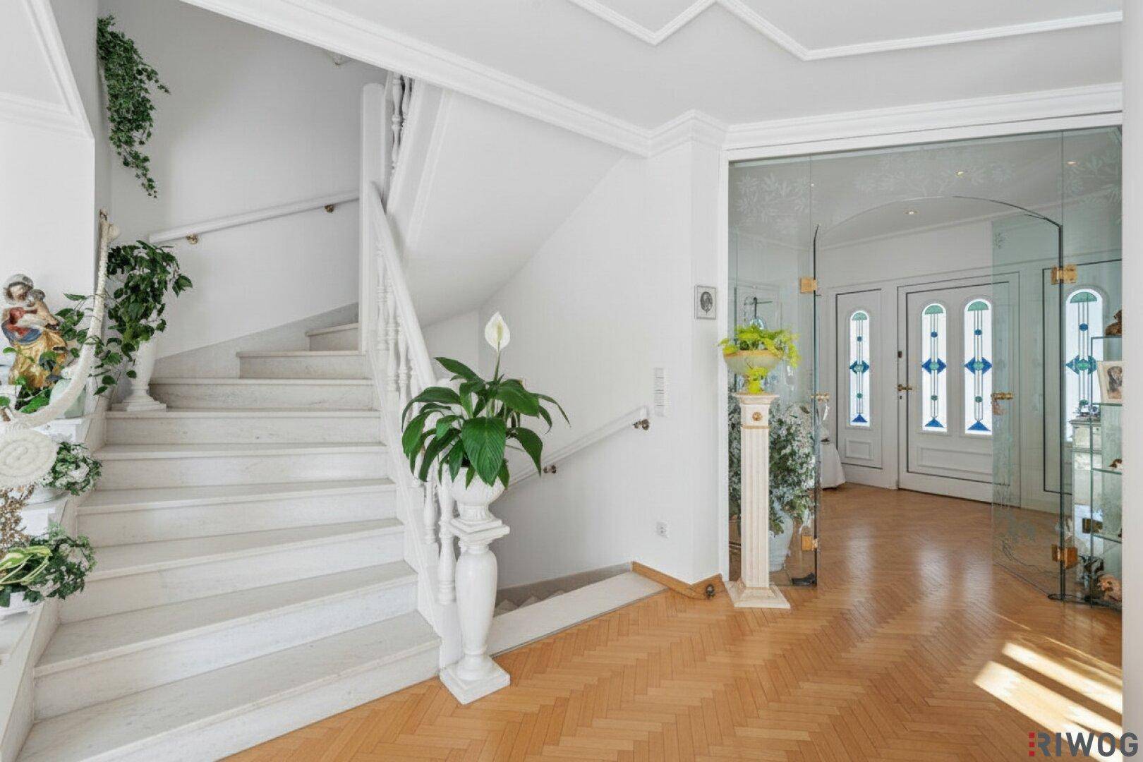 Eleganter Eingangsbereich mit Marmortreppe, Parkettboden und dekorativen Pflanzen.