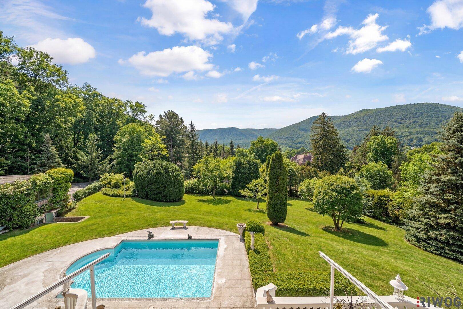 Weitläufiger Gartenbereich mit Pool, üppiger Vegetation und Panoramablick auf die Berge.