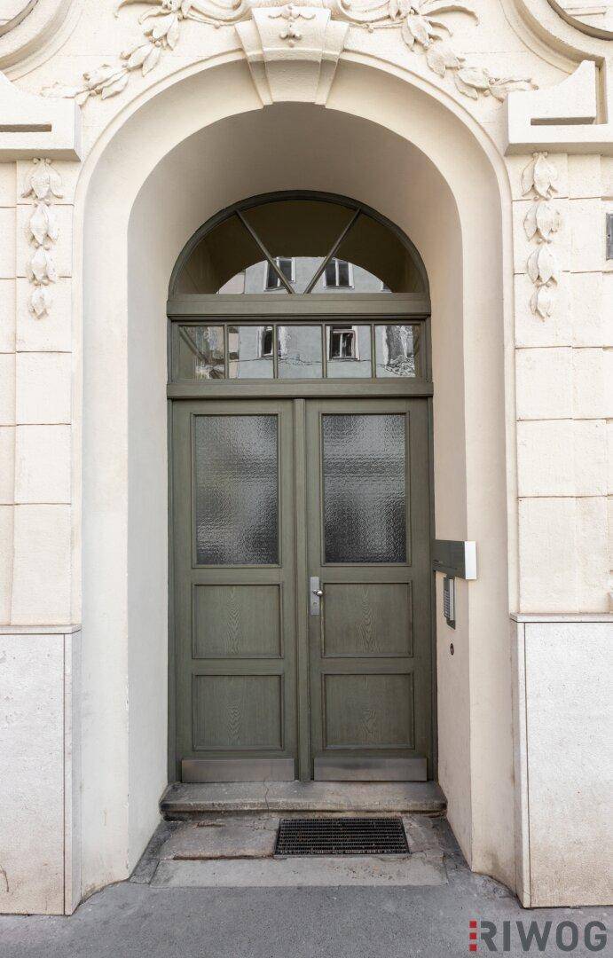 Historischer Haupteingang eines Altbaus mit Rundbogen und verzierten Details.