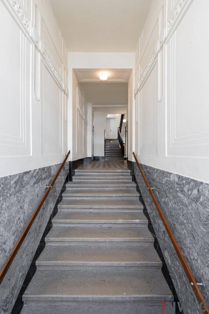 Weitläufiges Treppenhaus in einem historischen Gebäude mit Marmorwänden und Fliesenboden.