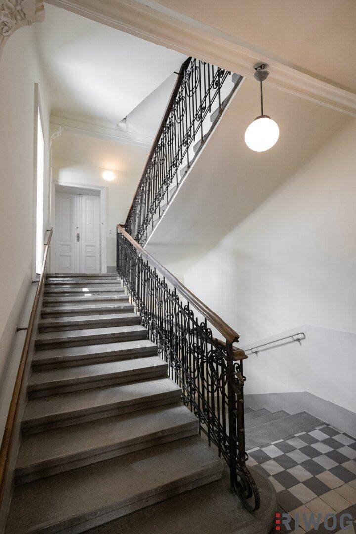 Großzügiges Treppenhaus in einem Altbau mit kunstvollem Geländer und klassischer Beleuchtung.
