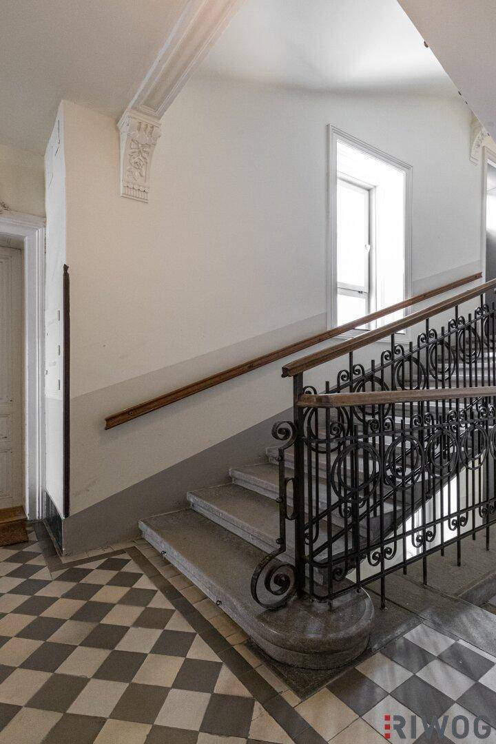 Historisches Treppenhaus mit Schachbrettmuster-Fliesen, schmiedeeisernem Geländer und Stuckverzierungen.