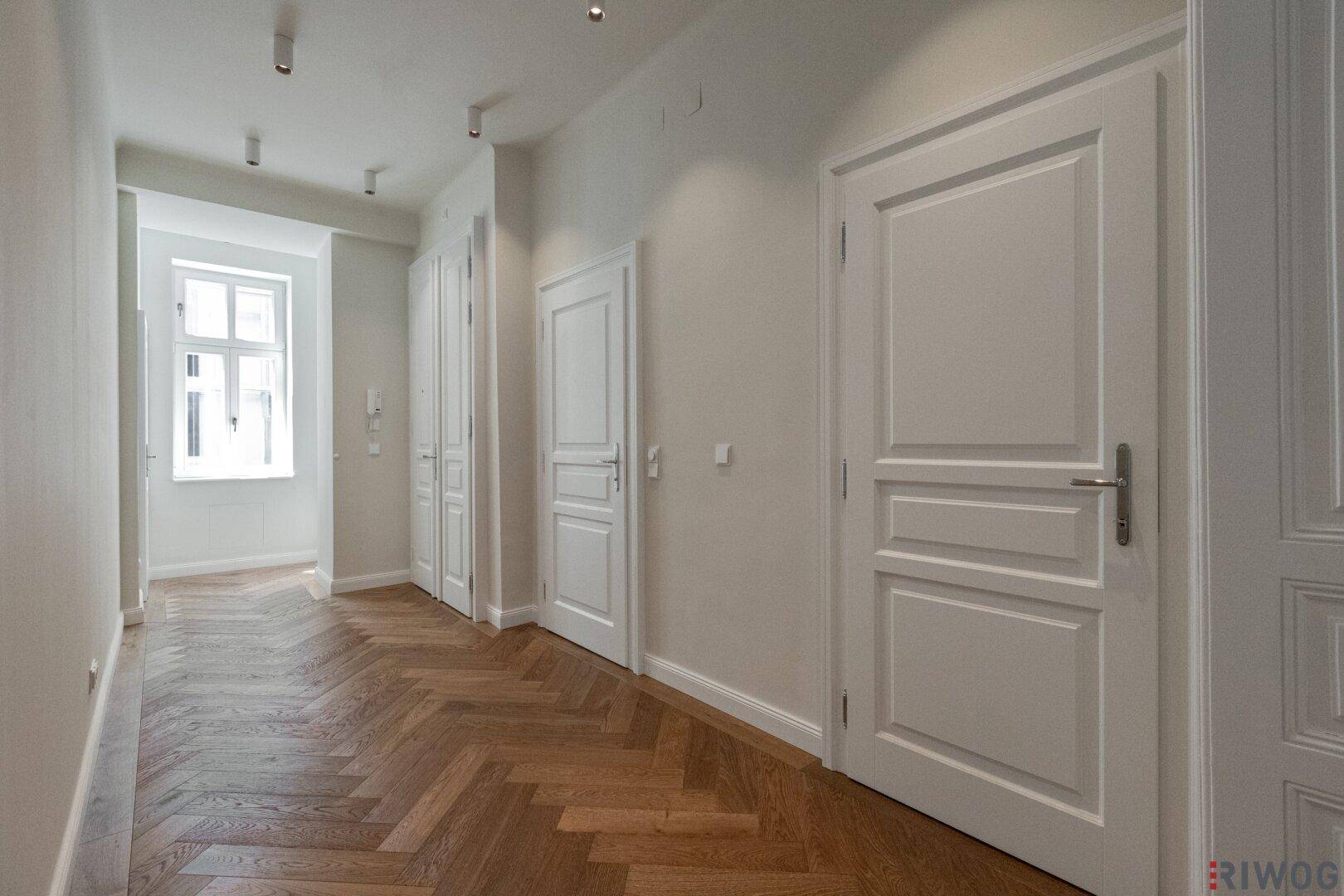 Geräumiger Flur mit elegantem Fischgrätparkett und klassischen weißen Türen, hell durch Fenster.