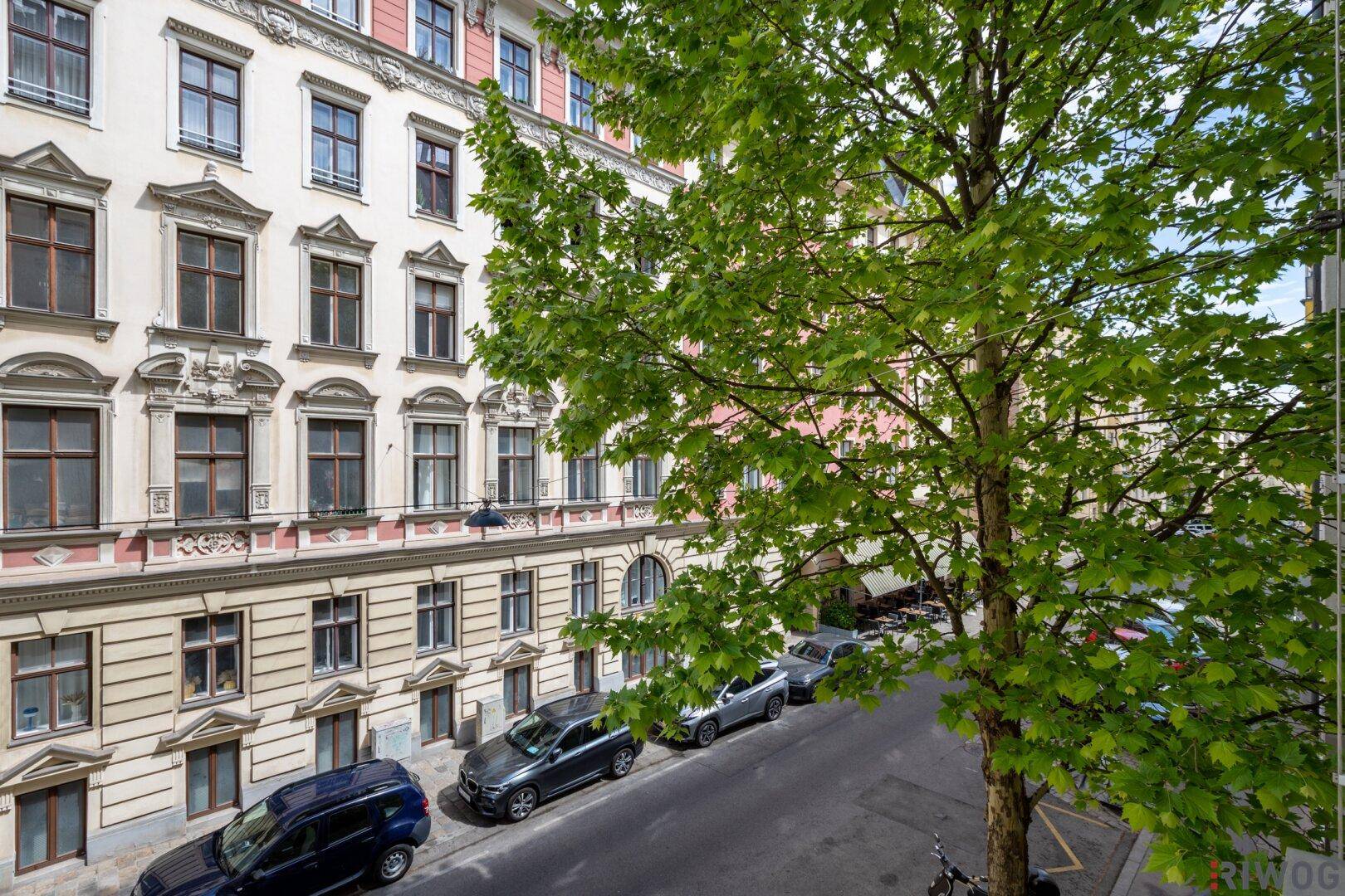 Historische Fassade eines Wohngebäudes mit Bäumen und parkenden Autos auf der Straße.