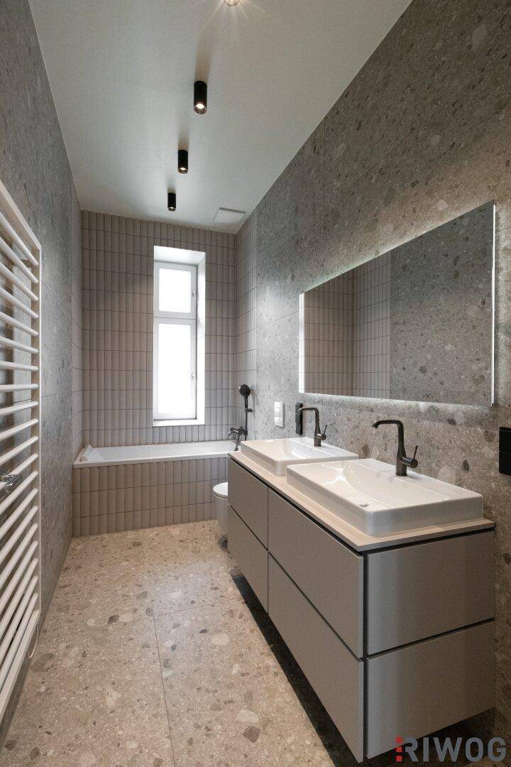 Modernes Badezimmer mit Doppelwaschbecken, beleuchtetem Spiegel und grauen Fliesen.