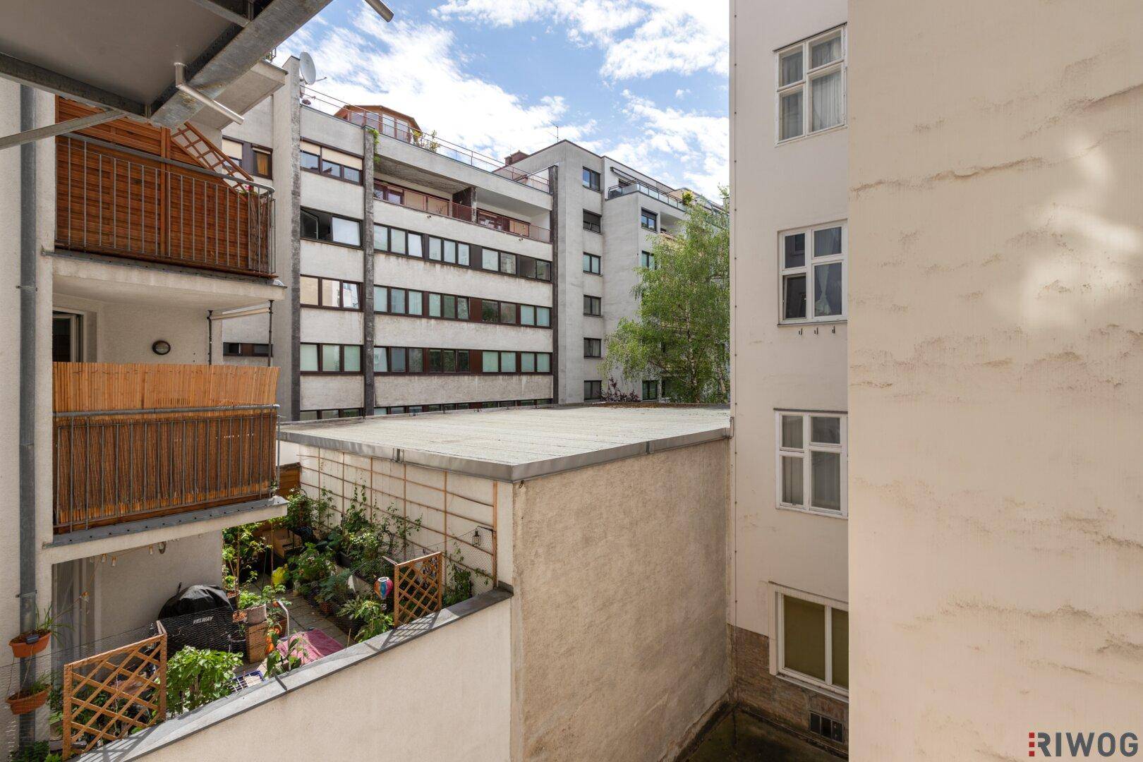 Blick von einem Balkon auf einen Innenhof mit Gärten und umliegenden Gebäuden.