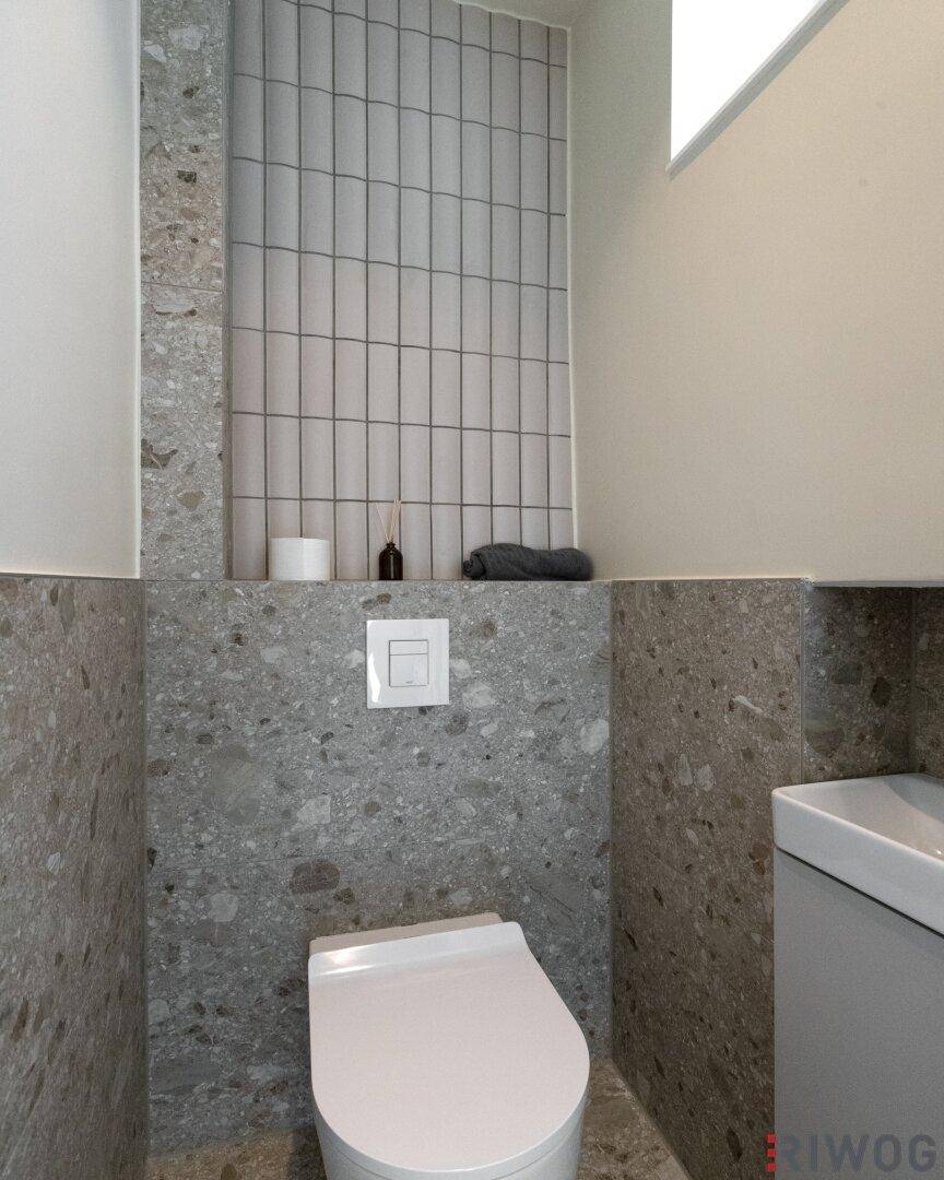Modernes Gäste-WC mit wandhängender Toilette und stilvollen grauen Fliesen.