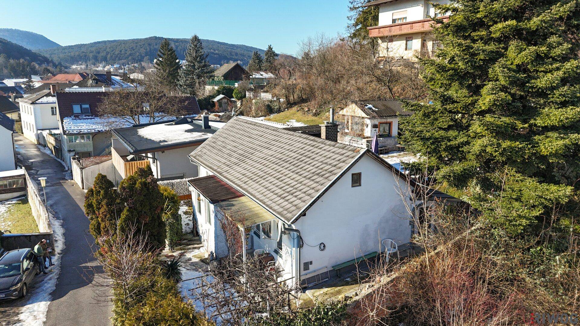 Blick auf das Einfamilienhaus mit umliegender Nachbarschaft und bewaldeten Hügeln im Hintergrund.