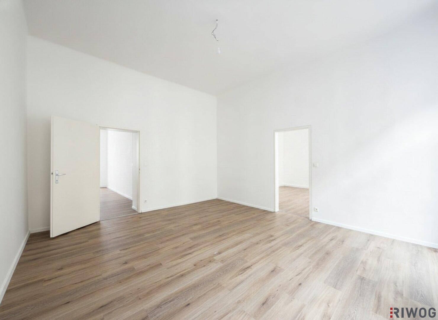 Heller Raum mit Holzboden und mehreren Türöffnungen, ideal für flexible Nutzung.