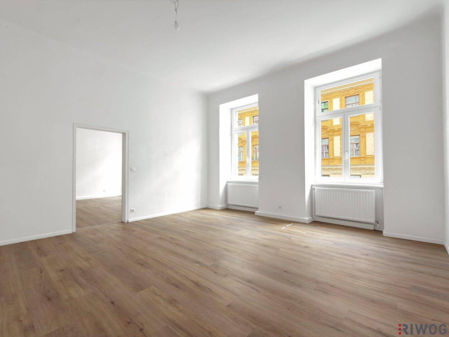 Geräumiger, heller Raum mit Holzboden und großen Fenstern, bereit zur individuellen Gestaltung.