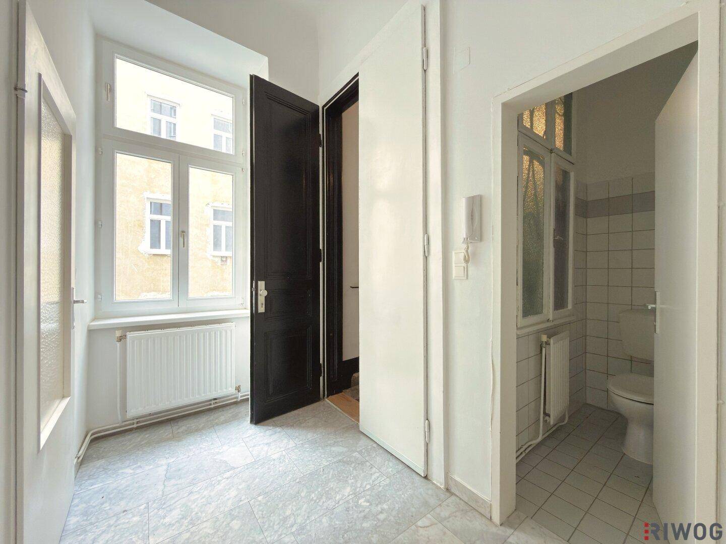 Heller Flur mit Fliesenboden und Zugang zu einem WC, mit Blick nach draußen.