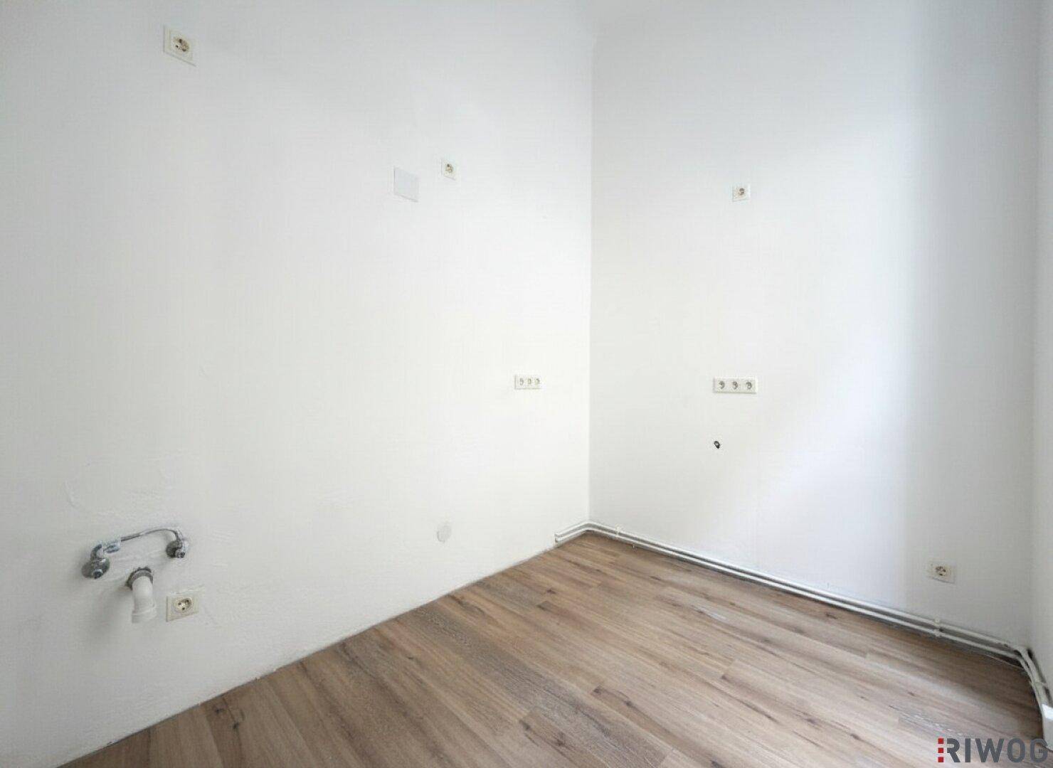 Leerer Küchenbereich mit Holzboden und Wandanschlüssen, ideal für eine moderne Küche.