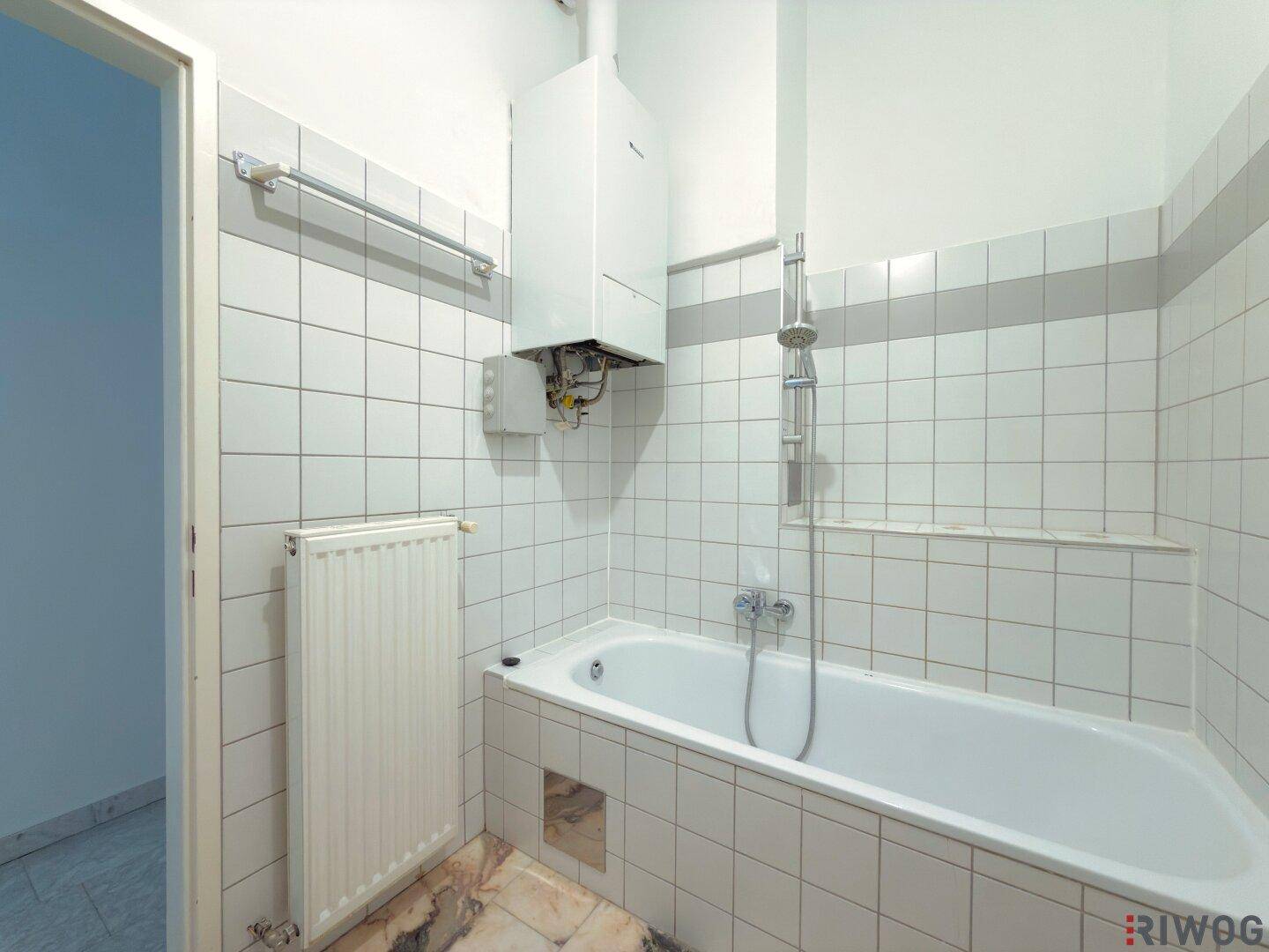 Badezimmer mit Badewanne, Duscharmatur und Heizkörper, in gutem Zustand.