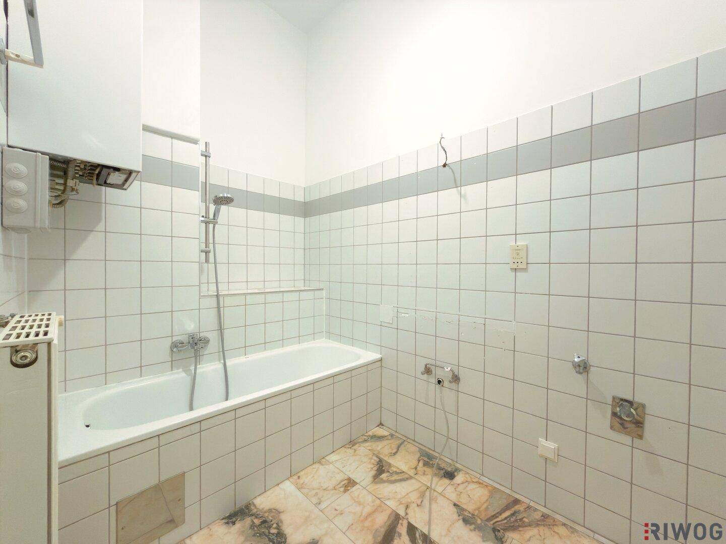 Badezimmer mit Badewanne, Fliesenwänden und Gastherme, bereit zur Modernisierung.