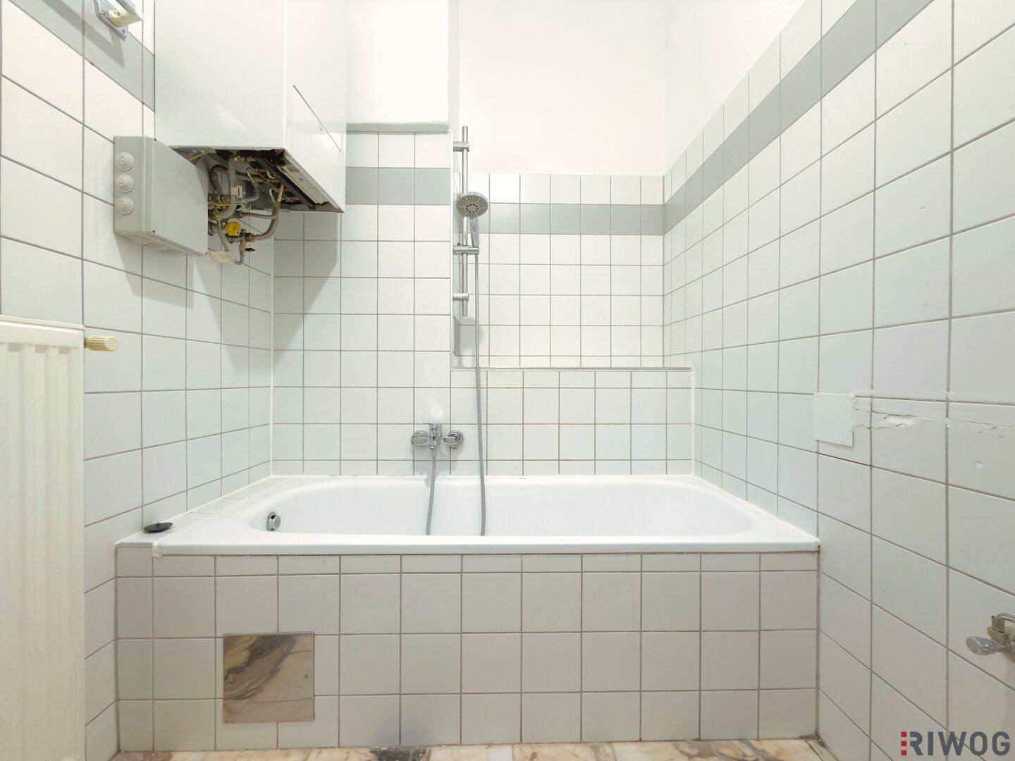 Badezimmer mit Badewanne und Duscharmatur, weißen Fliesen und Gastherme.