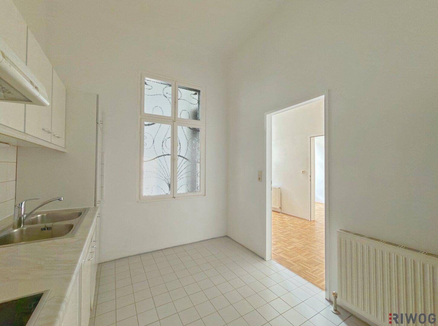 Küche mit Fliesenboden, Spülbecken und einem Fenster mit dekorativer Verglasung.