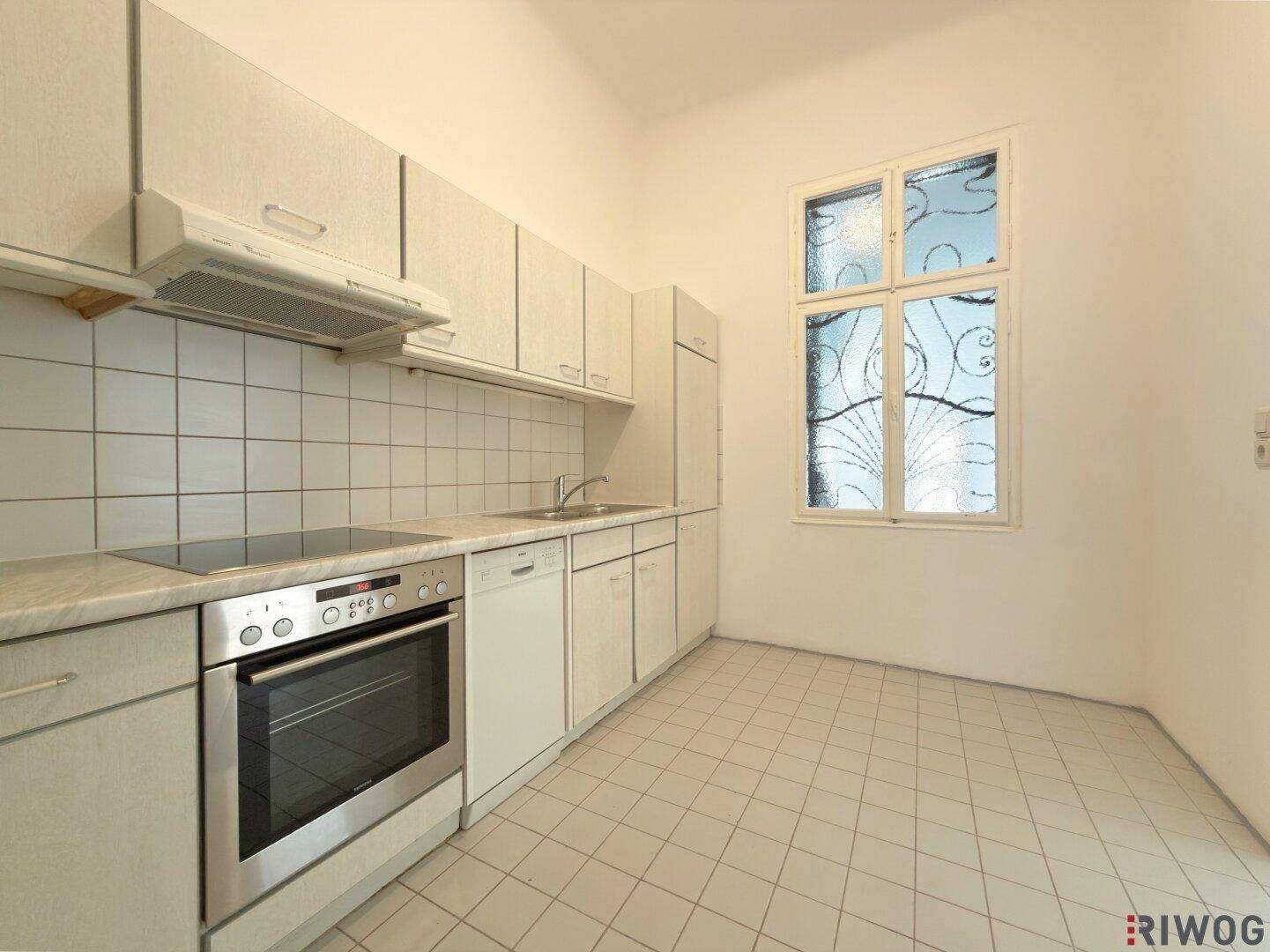 Küche mit Einbaugeräten, Fliesenboden und einem Fenster mit dekorativer Verglasung.