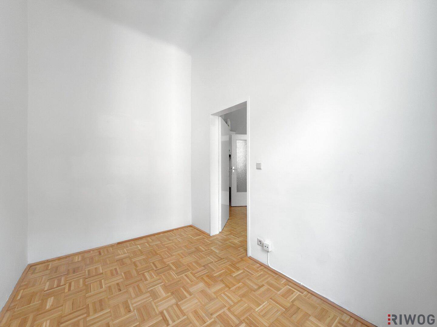 Leerer Raum mit Parkettboden und einem Durchgang zu einem weiteren Zimmer.