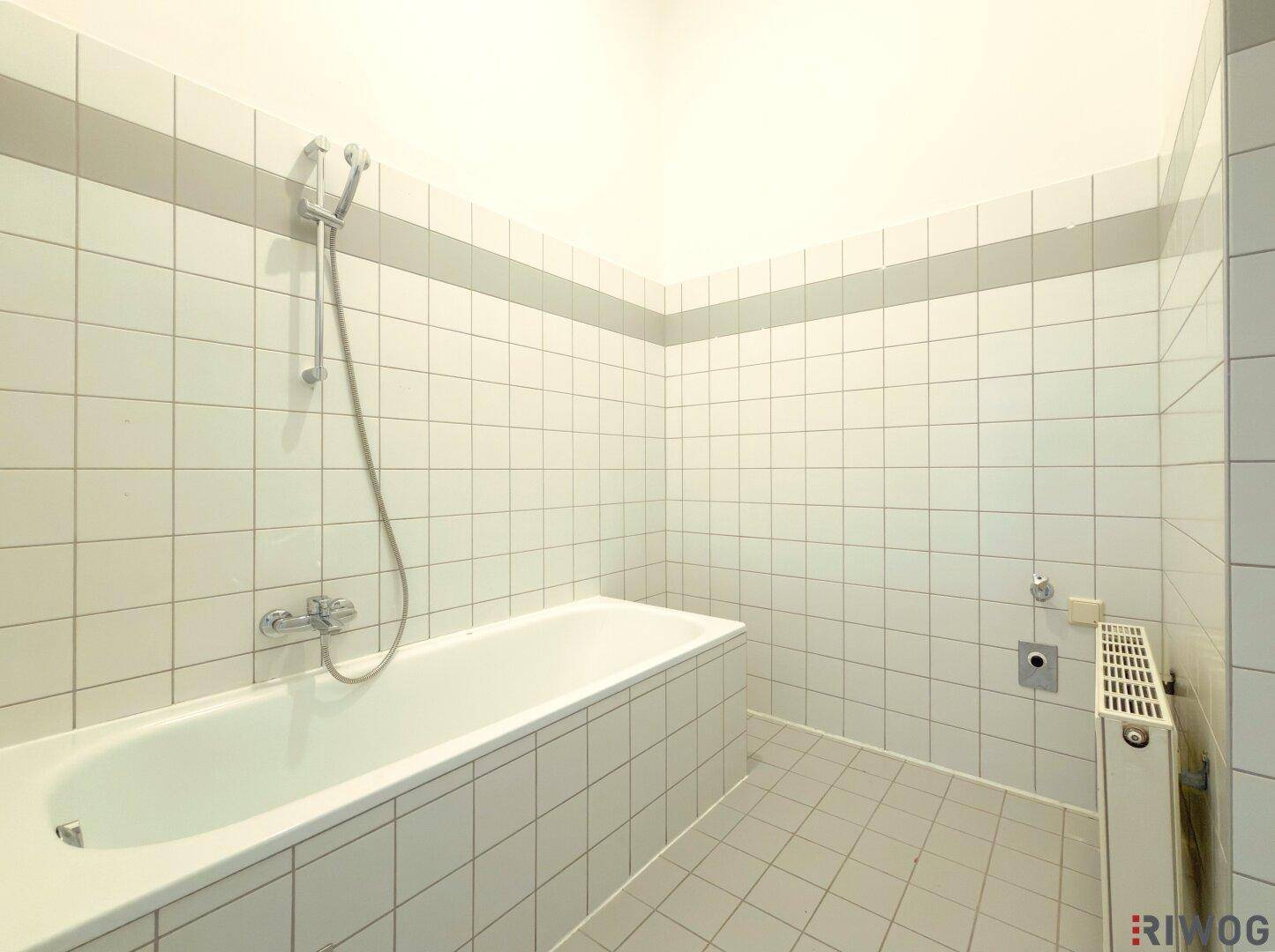 Badezimmer mit Badewanne und weißen Fliesen an Wänden und Boden.