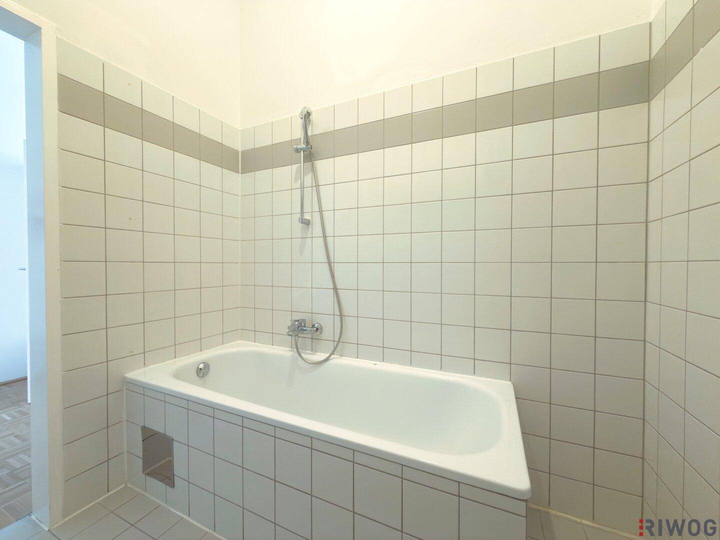 Badezimmer mit Badewanne und weißen Fliesen an Wänden und Boden.