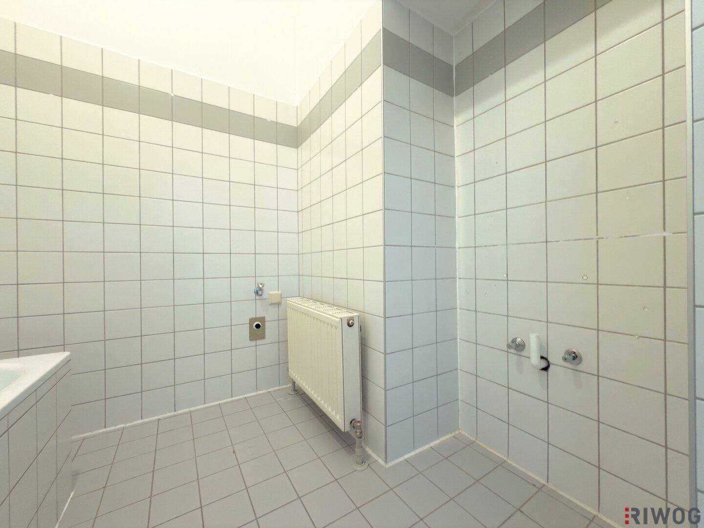 Gefliestes Badezimmer mit Heizkörper und Anschlüssen für weitere Sanitärobjekte.