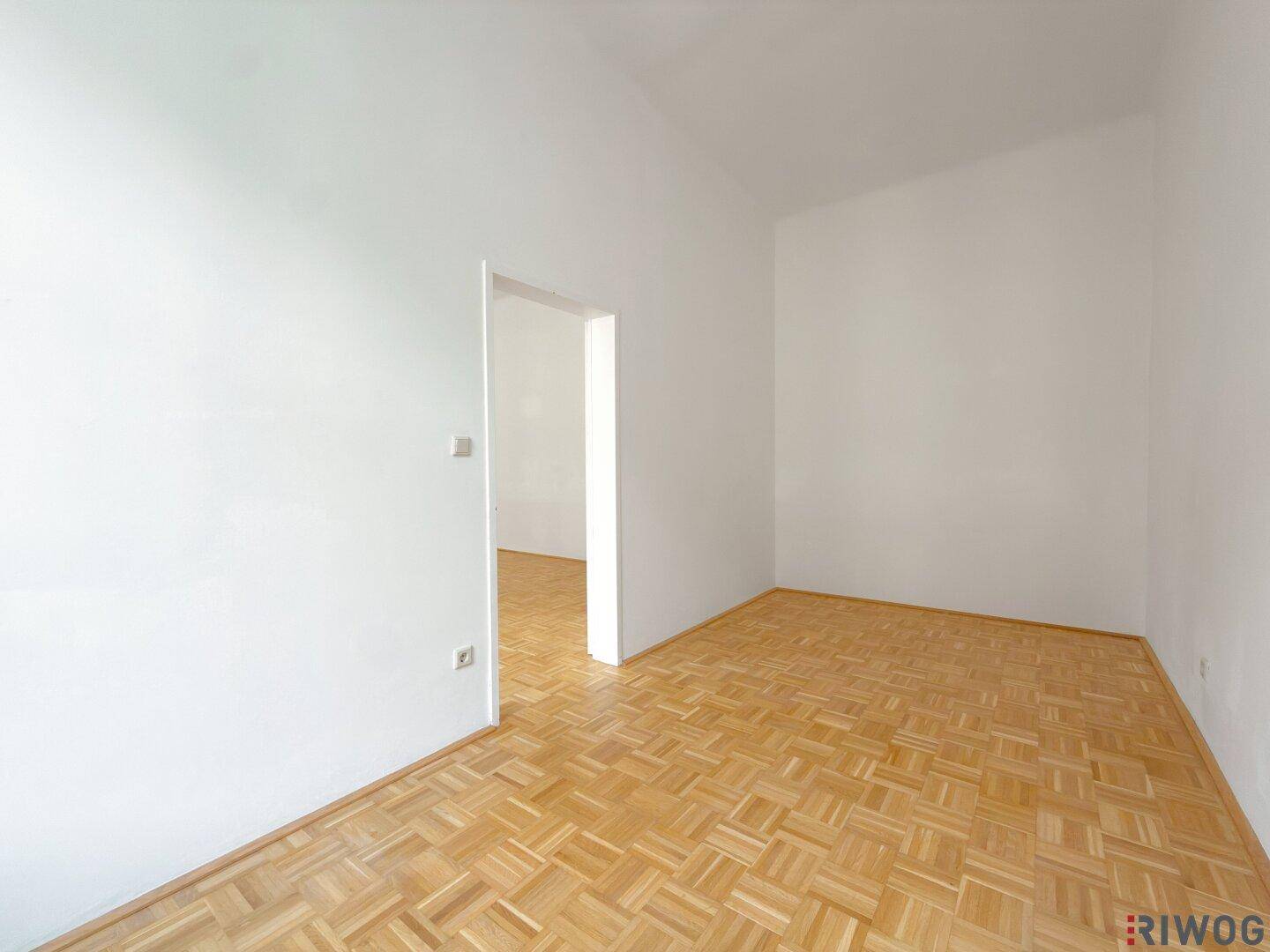 Leerer Raum mit Parkettboden und einem Durchgang zu einem weiteren Zimmer.