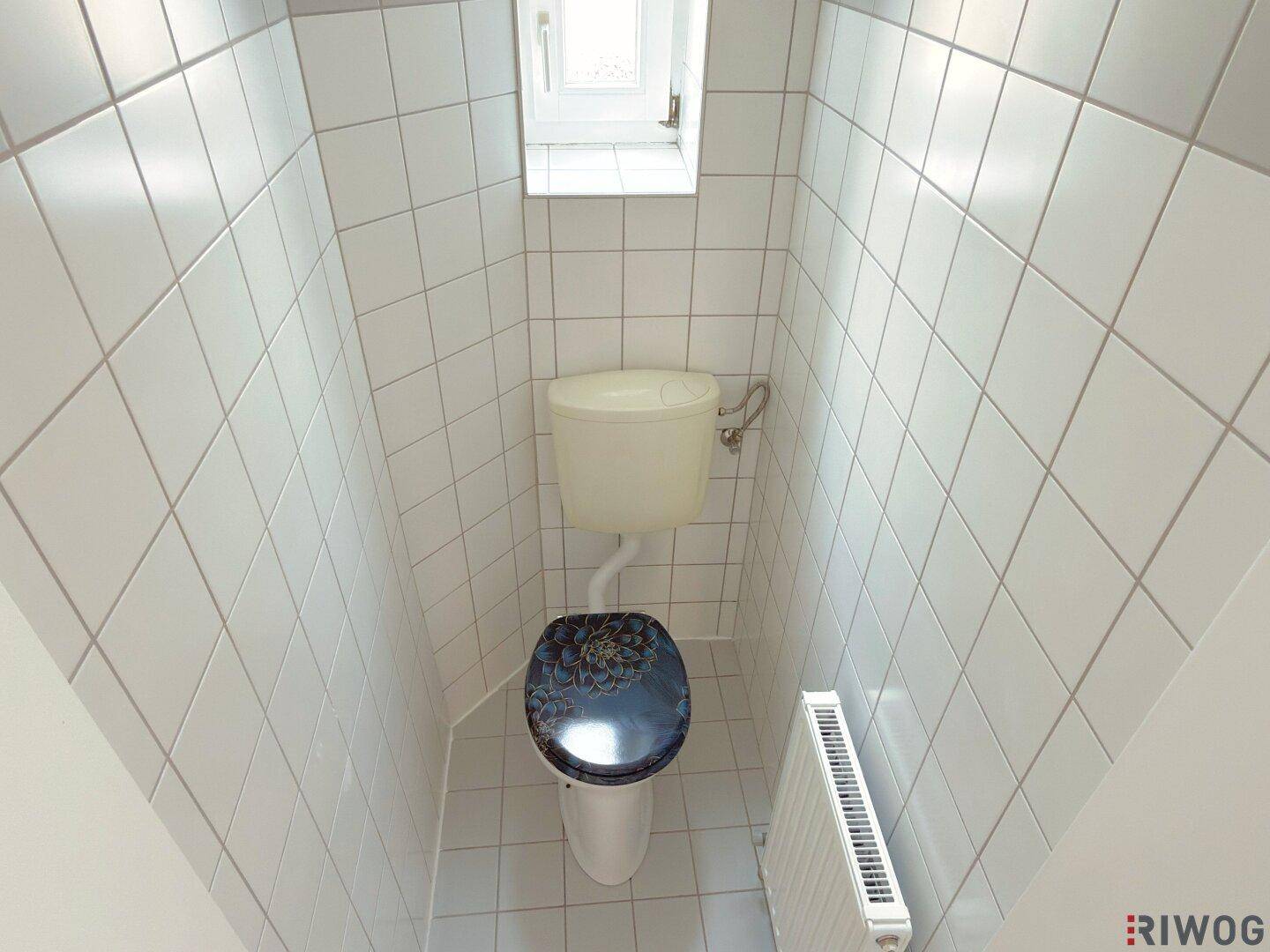 Separate Toilette mit Fenster, weißen Fliesen und einem Heizkörper.