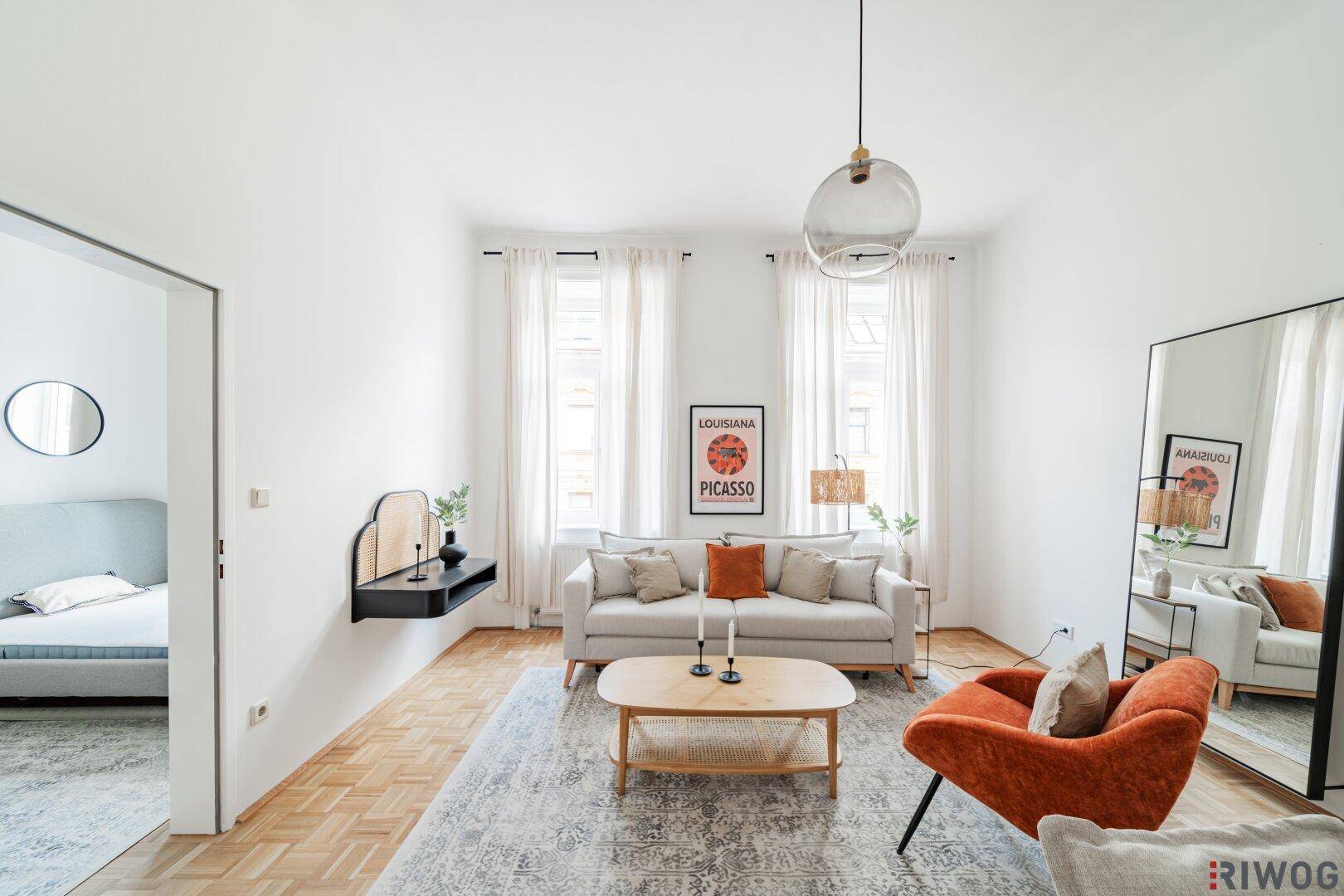 Helles Wohnzimmer mit Parkettboden, modernen Möbeln und Zugang zum Schlafzimmer.