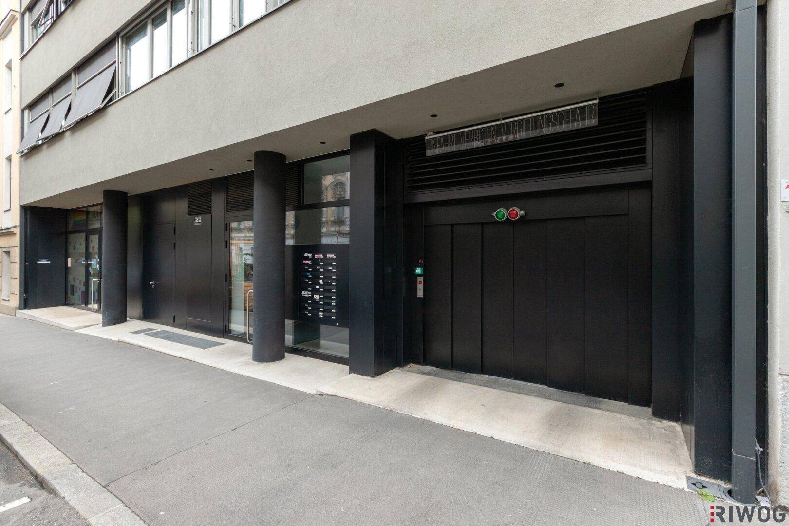 Gebäudeeingang mit schwarzer Aufzugstür und Briefkästen an der Fassade, im modernen Stil gehalten.