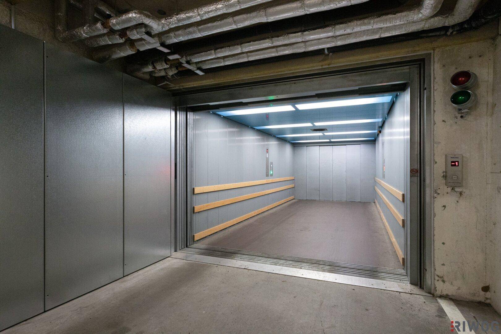 Innenansicht eines geräumigen Autoaufzugs mit Metallwänden und Holzschutzleisten, bereit zur Einfahrt.