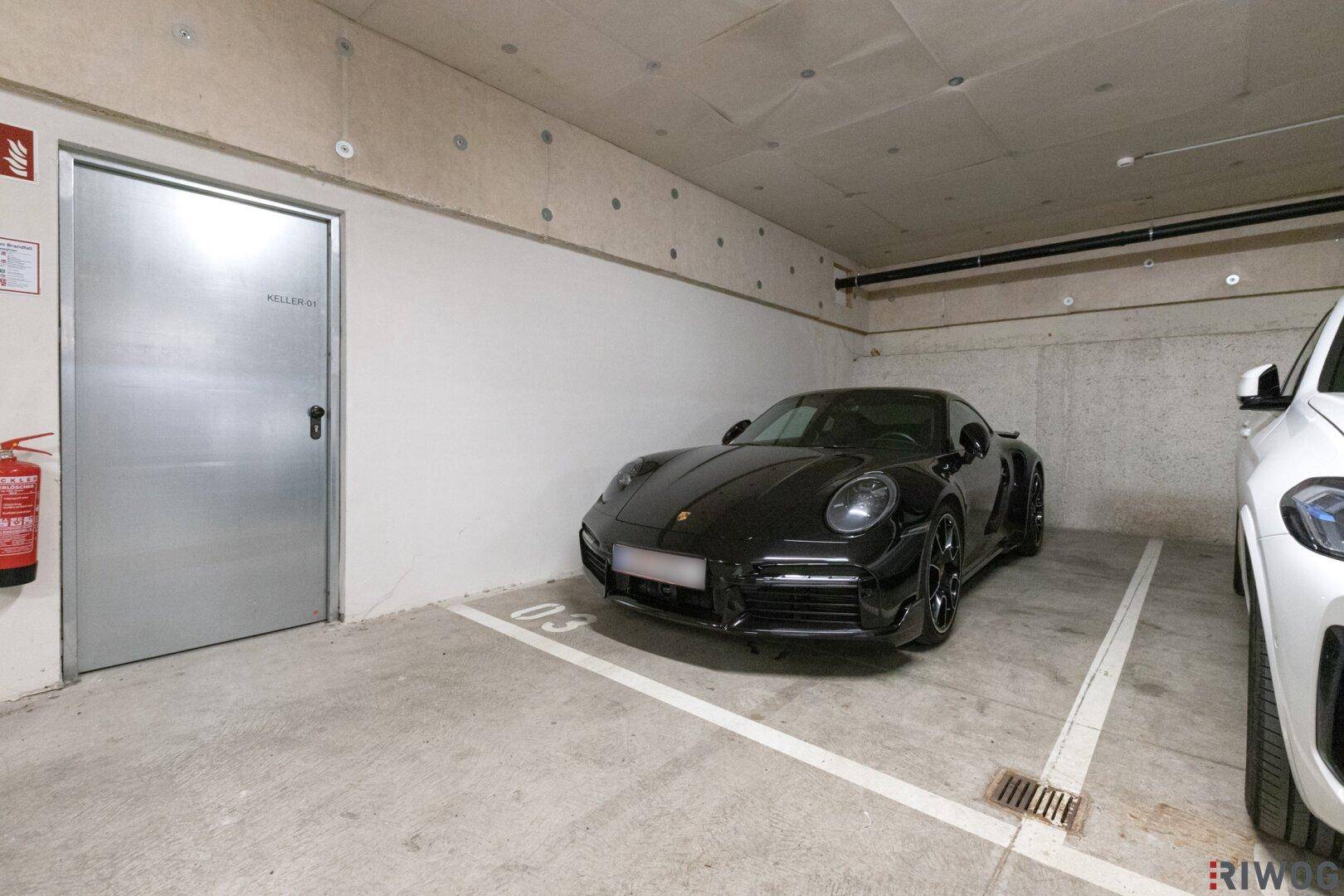 Tiefgaragenstellplatz mit einem Sportwagen und einer Stahltür, die zu einem Kellerraum führt.