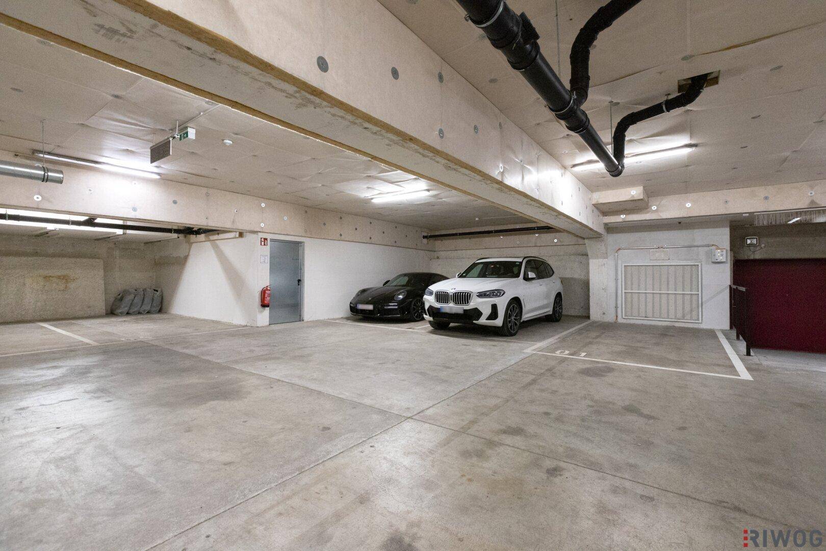 Tiefgarage mit zwei geparkten Autos, einer Kellertür und einem vergitterten Zugang, sauber und ordentlich.