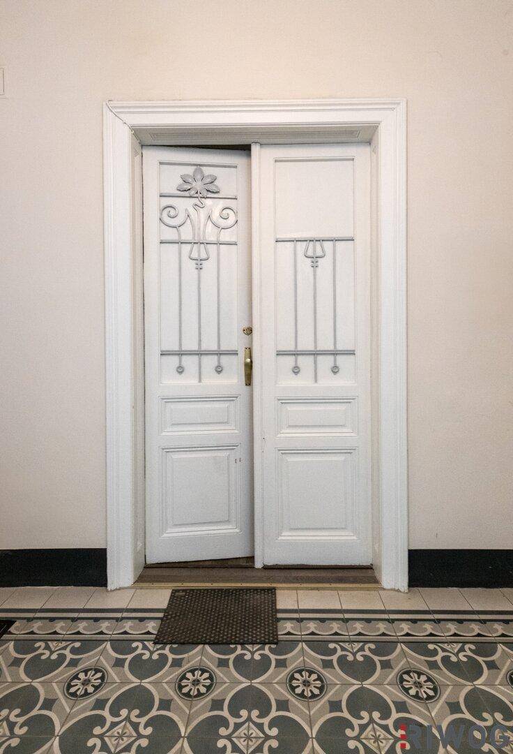 Eingangsbereich mit kunstvollen Doppeltüren und gemusterten Fliesen, die den Altbaucharme betonen.