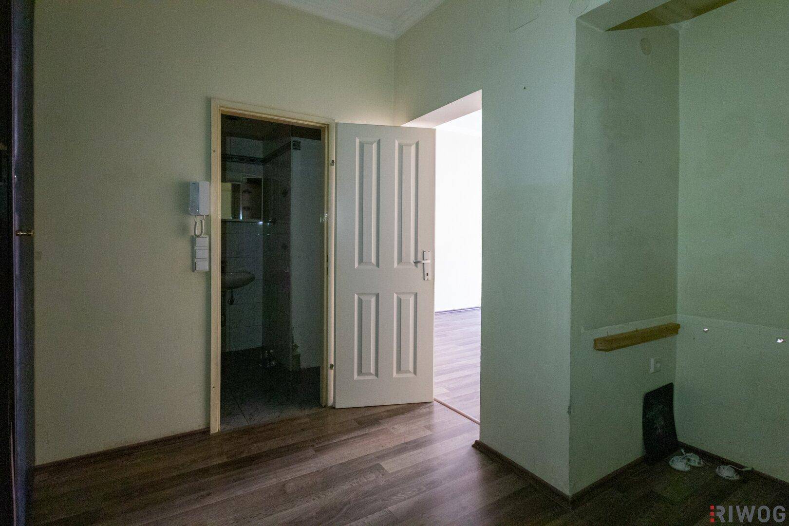 Flur mit Laminatboden und Zugang zu einem Badezimmer, das auf Renovierung wartet.