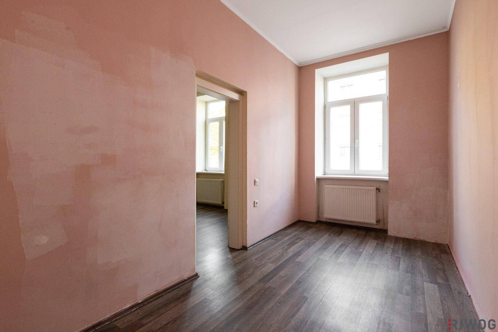 Unmöblierter Raum mit Laminatboden und rosa gestrichenen Wänden, ideal für ein Kinderzimmer.