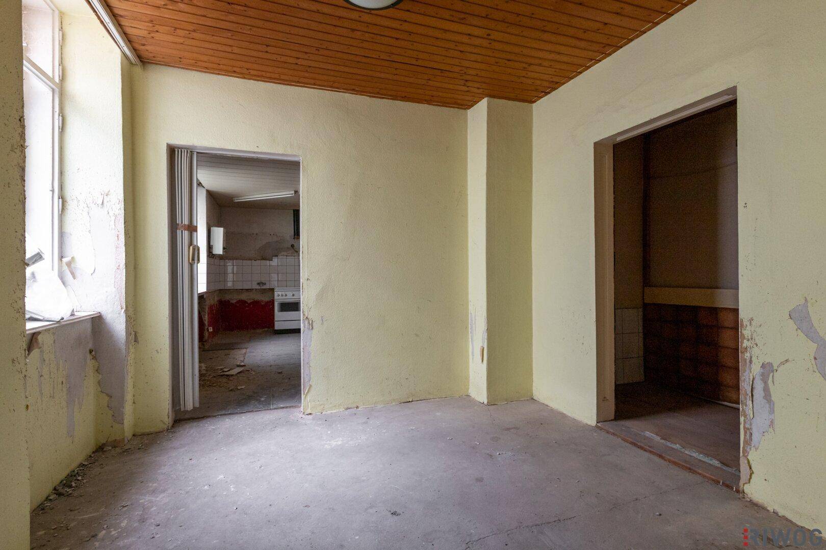 Flur mit Holzdecke und Blick in angrenzende Räume, der eine Renovierung benötigt.