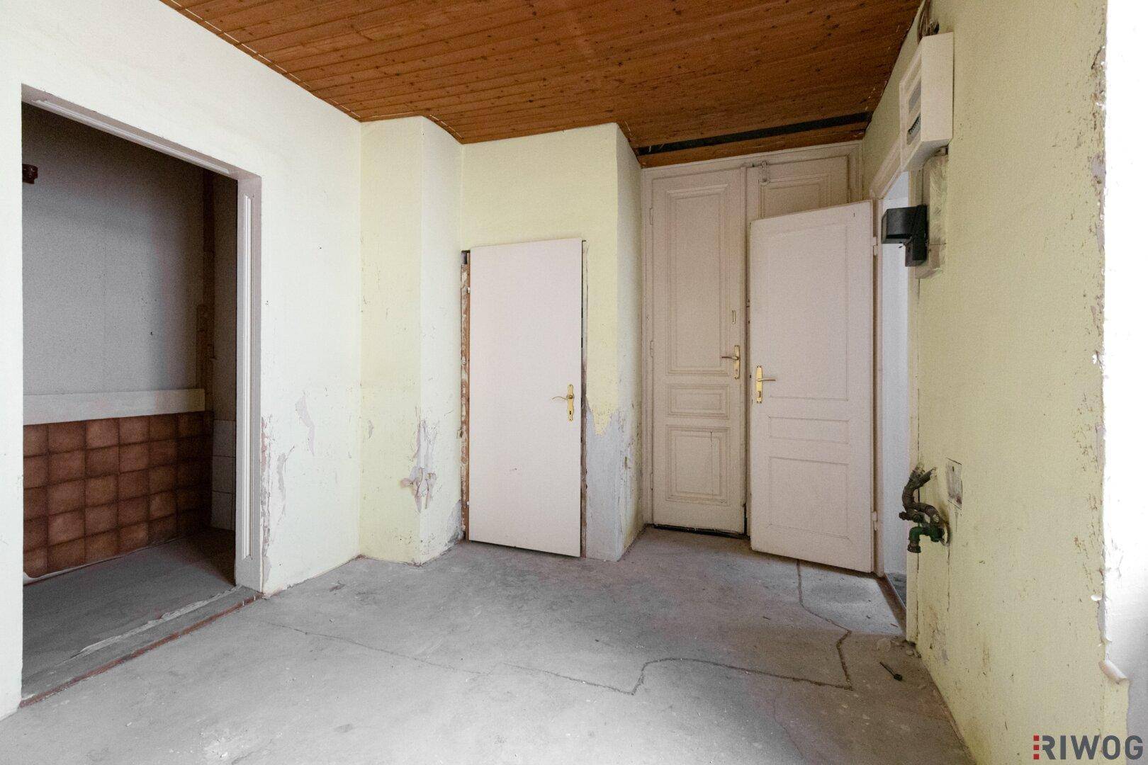 Abstellraum mit Holzdecke und mehreren Türen, der auf eine Renovierung wartet.