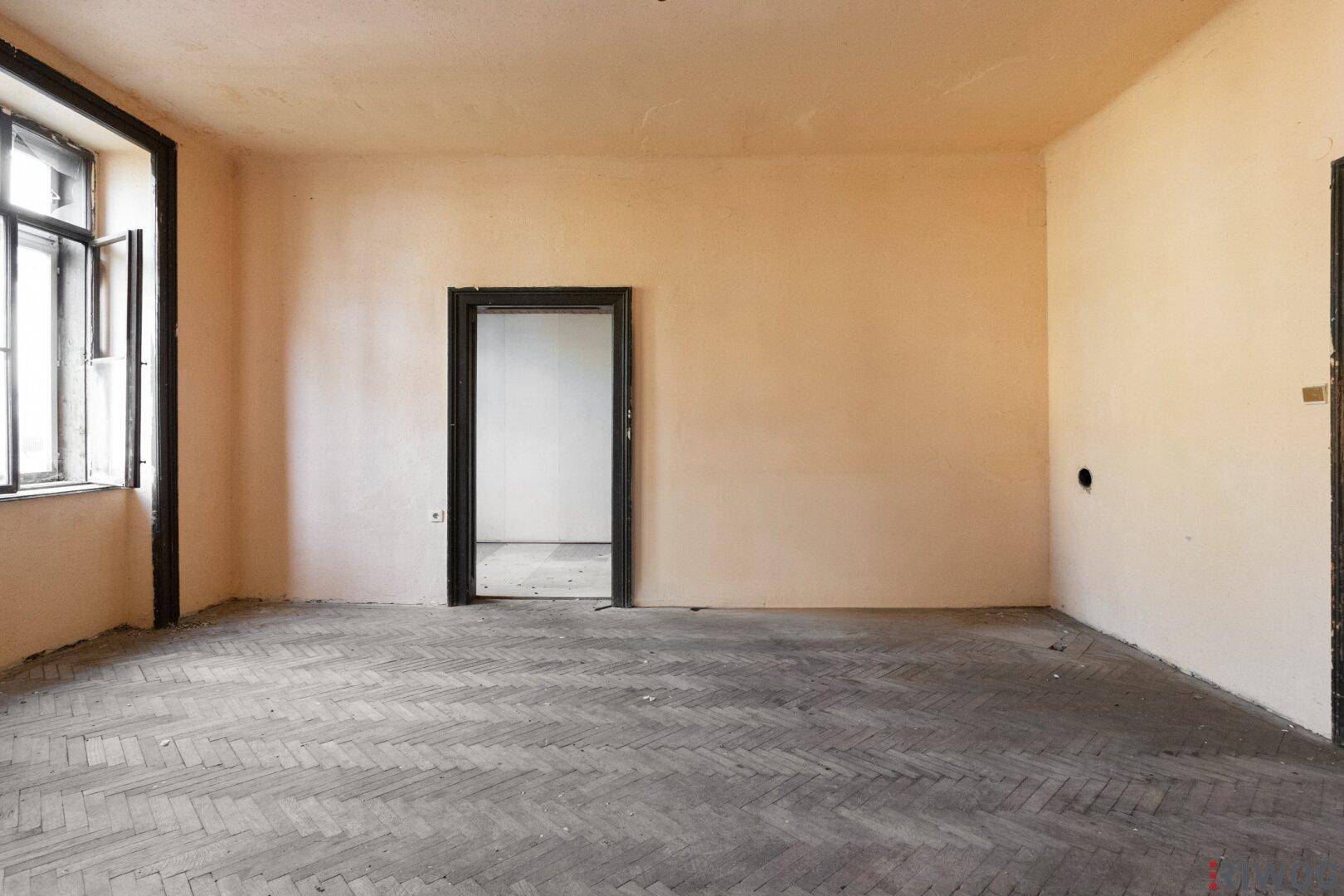 Geräumiges Zimmer mit altem Fischgrätparkett und hohen Decken, bereit für eine umfassende Renovierung.