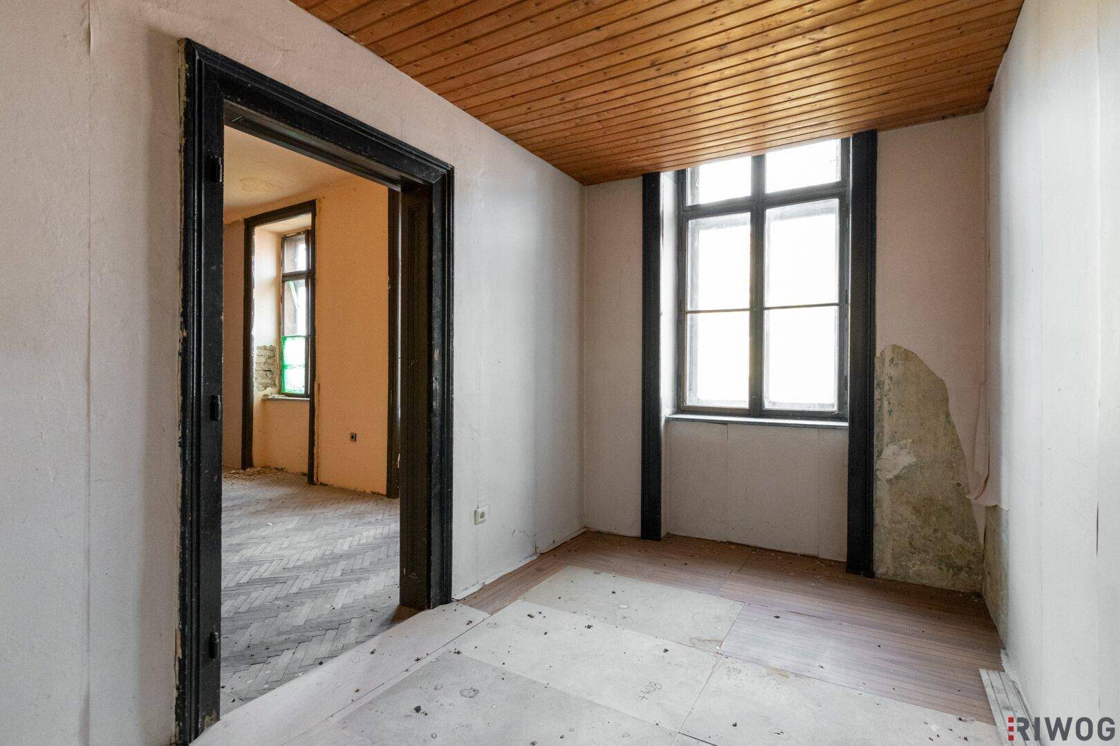 Kleiner Raum mit Holzdecke, Fenster und abgenutzten Wänden, der auf eine Renovierung wartet.