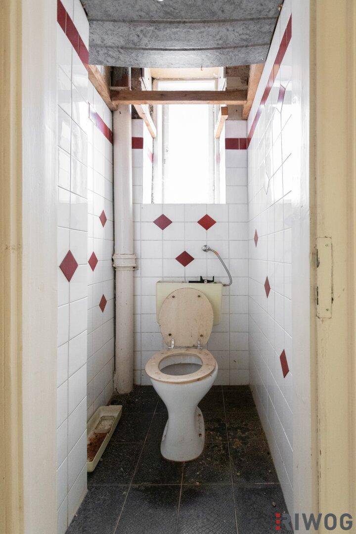 Kleines WC mit Fliesen, Fenster und einfacher Toilette, renovierungsbedürftig.