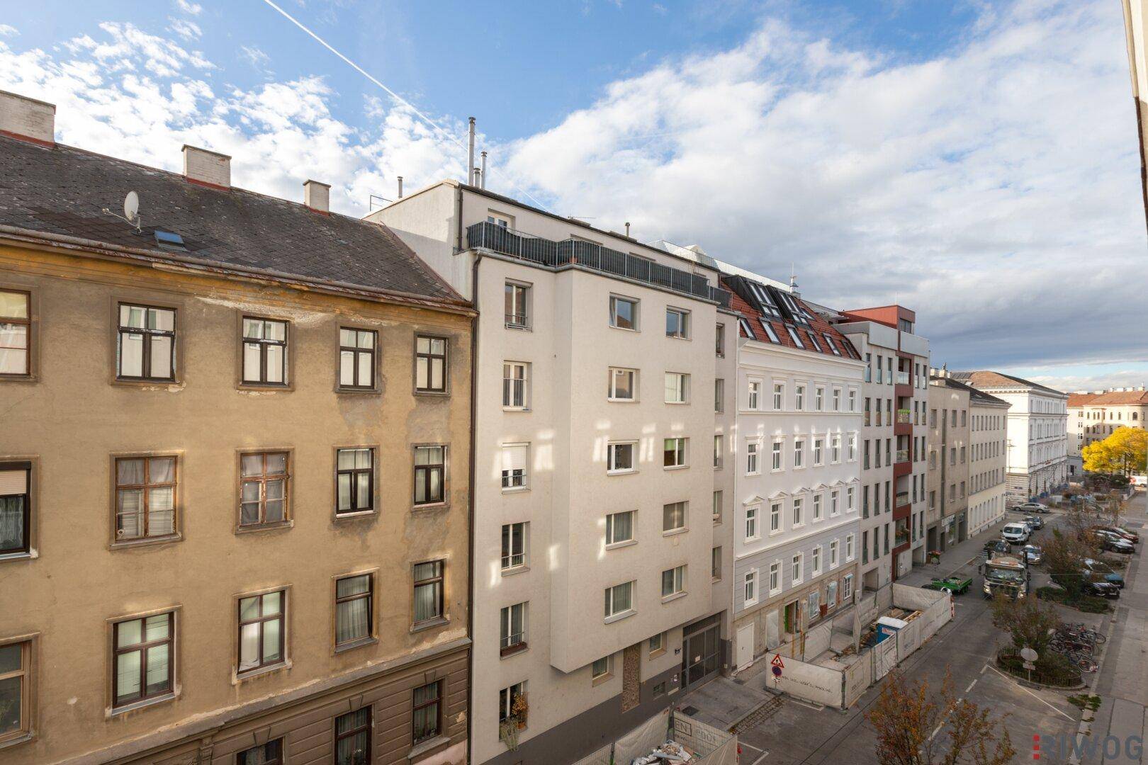 Panoramablick auf eine städtische Straße mit verschiedenen Gebäudefassaden unter bewölktem Himmel.