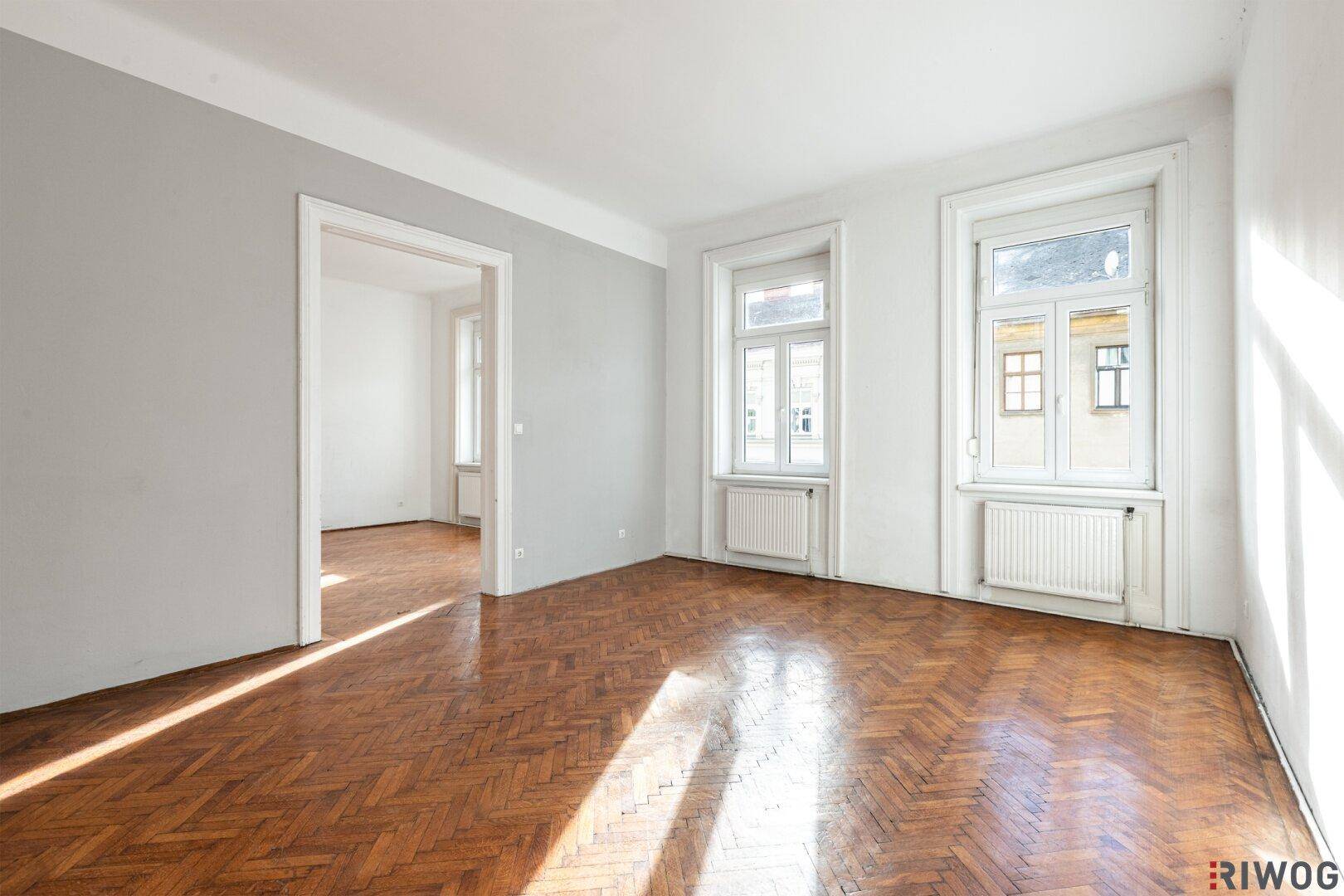 Helles, leeres Zimmer mit Fischgrätparkett und einer grauen Akzentwand, bereit zur Gestaltung.