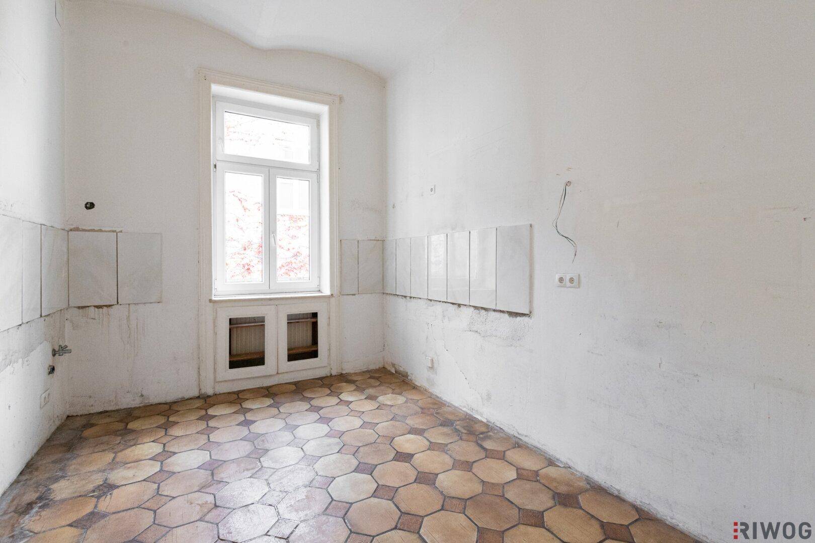 Leere Küche mit alten Fliesen und vorbereiteten Wänden für eine neue Kücheninstallation.